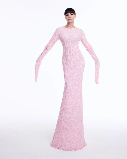 Elegant woman poses in a pink, textured gown against a white background, creating a clean, high-fashion studio shot with minimalist appeal.