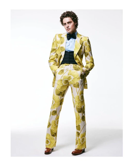 Man in a floral suit stands in a full shot on a white background. He wears a light blue dress shirt and a black bow tie.