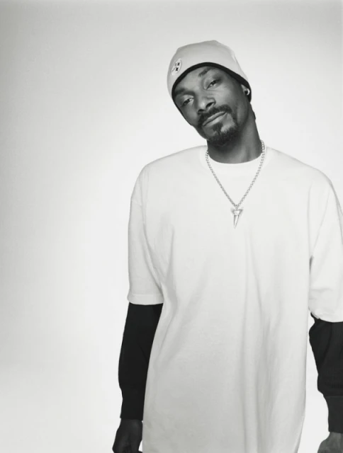 Monochromatic portrait of Snoop Dogg wearing a beanie and a white t-shirt with a silver shark-tooth pendant necklace.