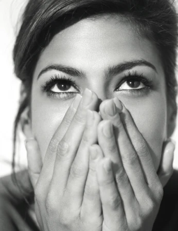 Close-up monochrome portrait of a woman looking upward with hands held loosely covering her lower face, photographed by Sheryl Nields.