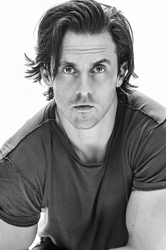 Black-and-white portrait of an adult male with medium-length hair looking directly at the camera, wearing a t-shirt against a white background.