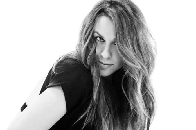 Portrait of a woman with long wavy hair looking back over her shoulder against a plain white background