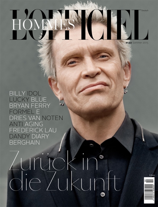Magazine cover featuring a portrait of Billy Idol in a black collared shirt and blazer against a blurry gray background, with bold text.