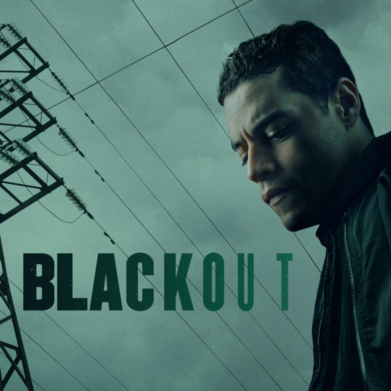 Portrait of a man with a serious expression, looking down, set against an electrical tower with power lines and the word 'BLACKOUT'.