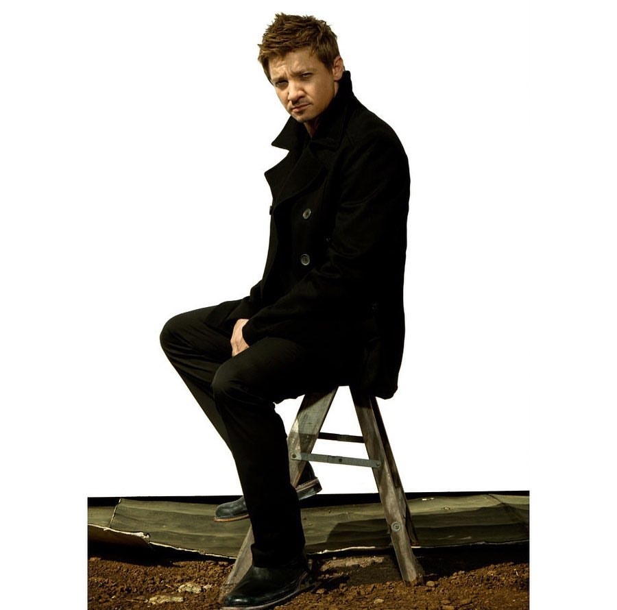 Adult male poses on a ladder in a photo studio wearing a black jacket and black pants on a dark surface against a white background.