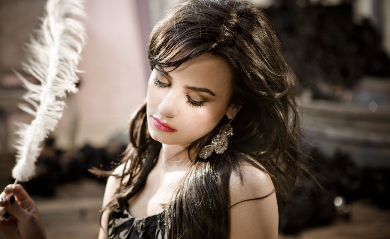 Demi Lovato holding a white feather in a close-up portrait photographed by Sheryl Nields