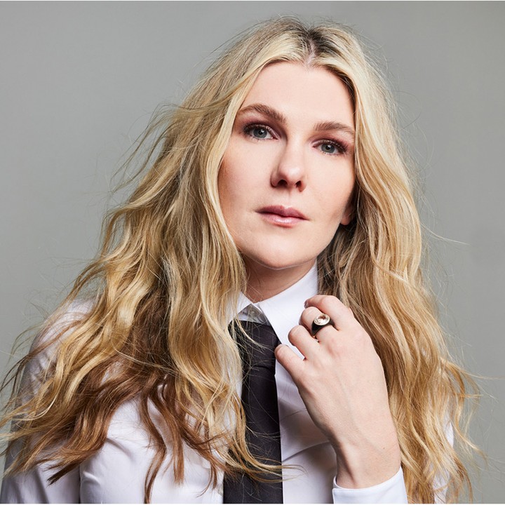 Portrait of a blonde woman wearing a white shirt and black tie with a ring on her finger