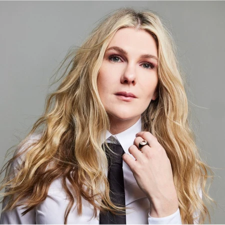 Portrait of a blonde woman wearing a white shirt and black tie with a ring on her finger