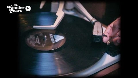Close-up of a person's hand lowering the needle onto a vinyl record on a turntable, with 'The Wonder Years' logo in the corner.