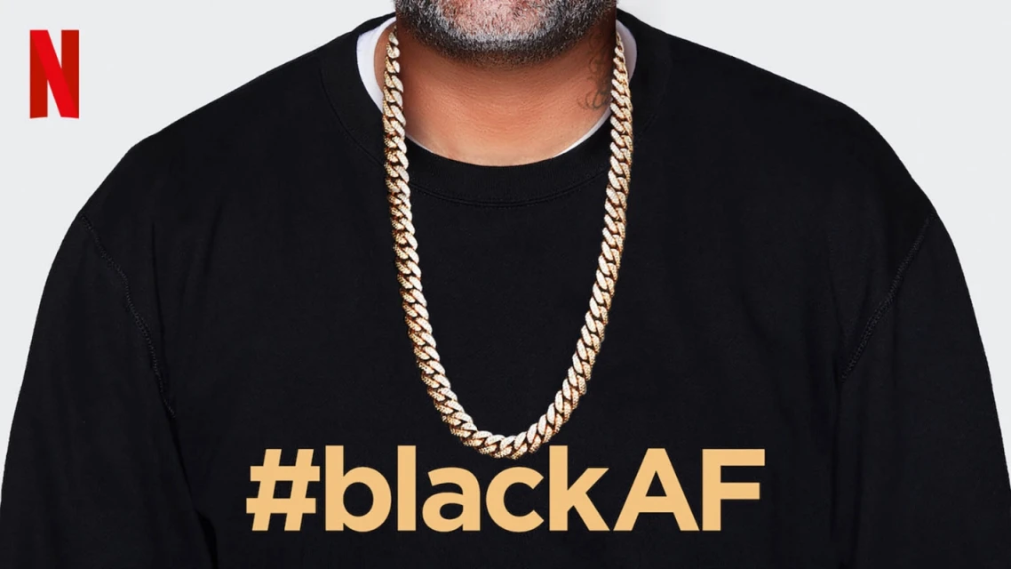 Close-up of an adult wearing a black crewneck sweatshirt with '#blackAF' in gold text, a gold chain, and a visible tattoo on the neck.