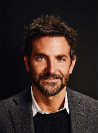 Close-up portrait of Bradley Cooper with a beard wearing a grey tweed jacket and white collared shirt against a dark background