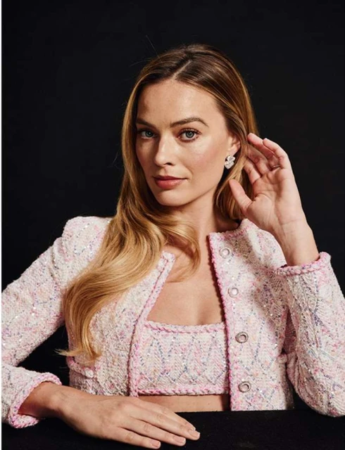 Close-up portrait of a blonde woman in a light pink jacket and top, posing in a studio with a black background and soft lighting.