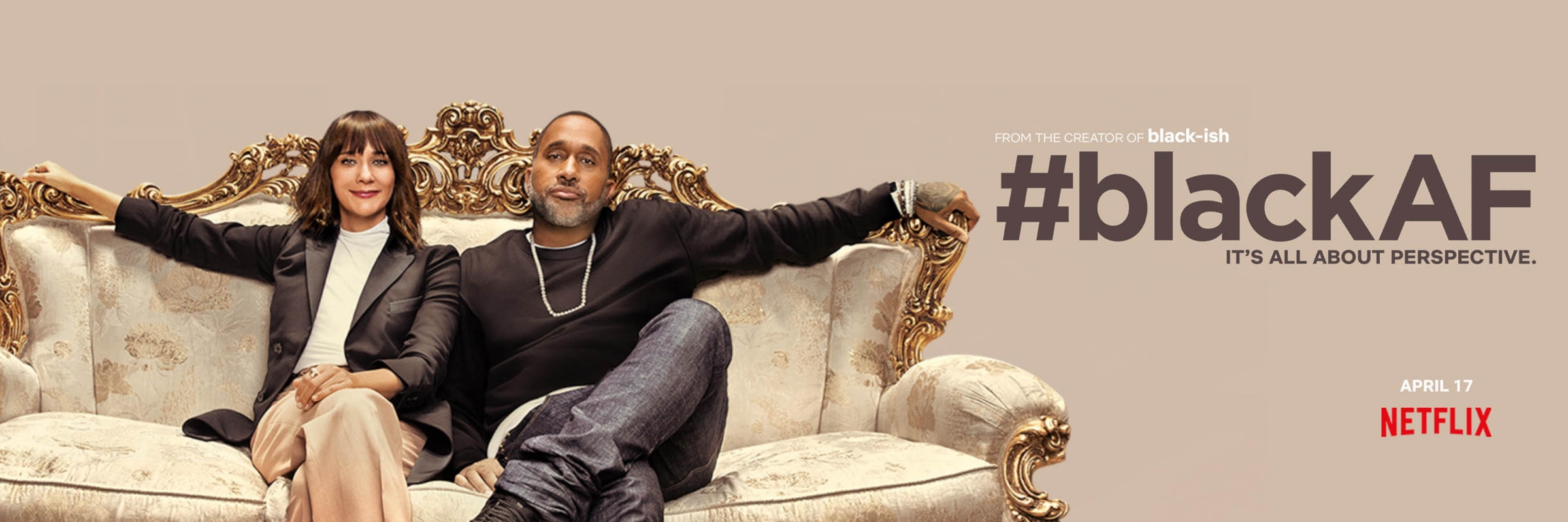 Rashida Jones and Kenya Barris seated together on an ornate carved sofa against a neutral background for BlackAF by Matt Sayles