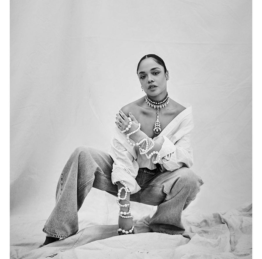 Portrait of an adult woman in a studio setting, wearing pearl jewelry with an off-the-shoulder shirt and denim jeans, black and white.