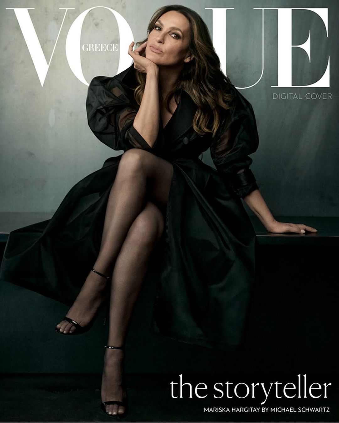 Mariska Hargitay on Vogue Greece cover in a black dress, seated with legs crossed, long hair, and hand on chin, in a studio setting.