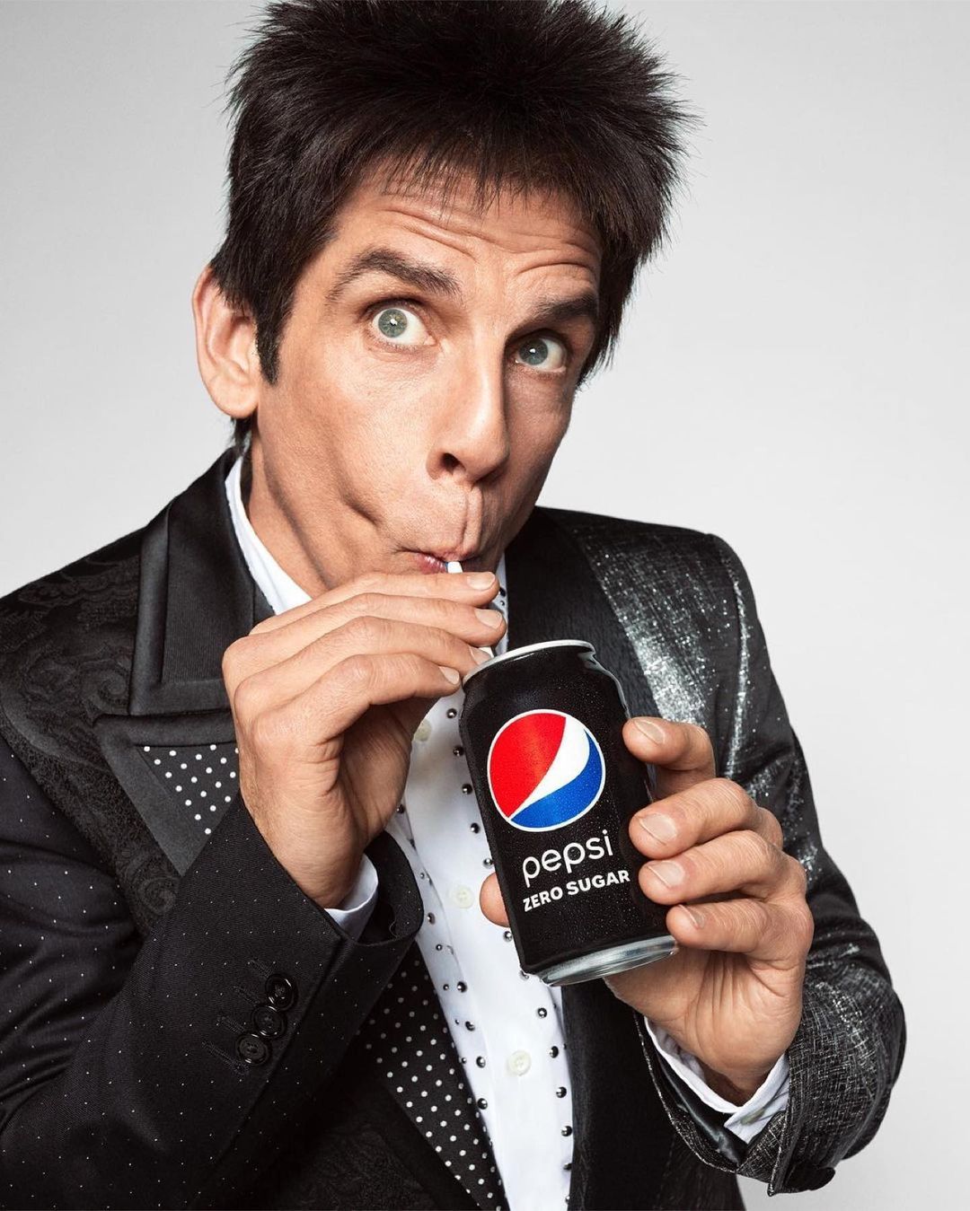Adult male in formal wear drinks Pepsi Zero Sugar from a can with a straw in a photo studio setting.