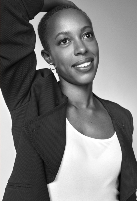 Black-and-white portrait of a smiling woman with short hair wearing a dark jacket and light top, photographed by Michael Schwartz.