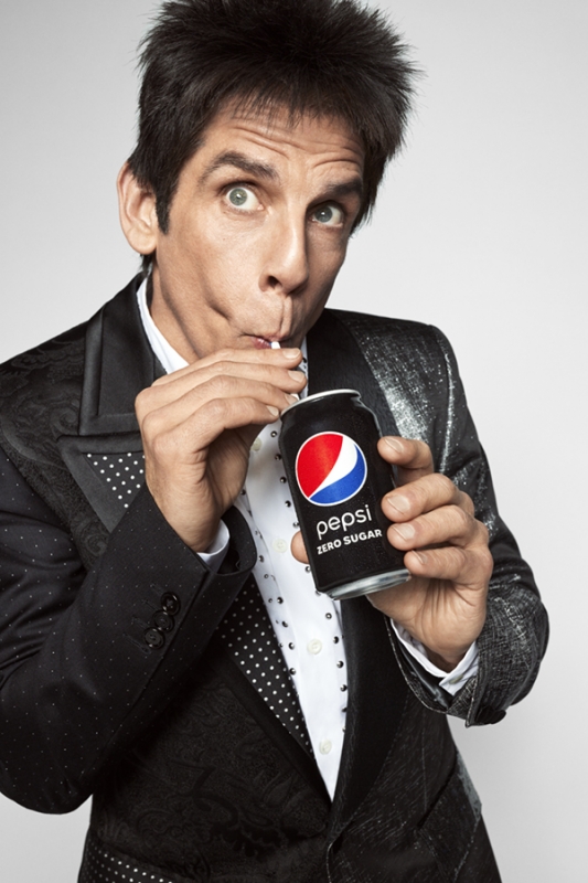 Adult male in sparkly black suit sips Pepsi Zero Sugar through straw against white background. Beverage, lifestyle, and celebrity.
