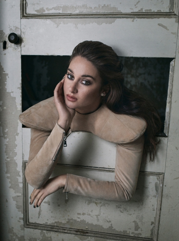Brunette woman with long hair posing in a doorway wearing a tan collared jacket. The frame is distressed and painted white.