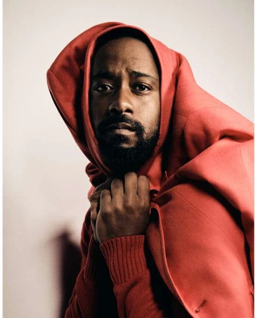 Portrait of African-American man in bright red hooded coat against neutral backdrop, captured in a medium shot with soft lighting.