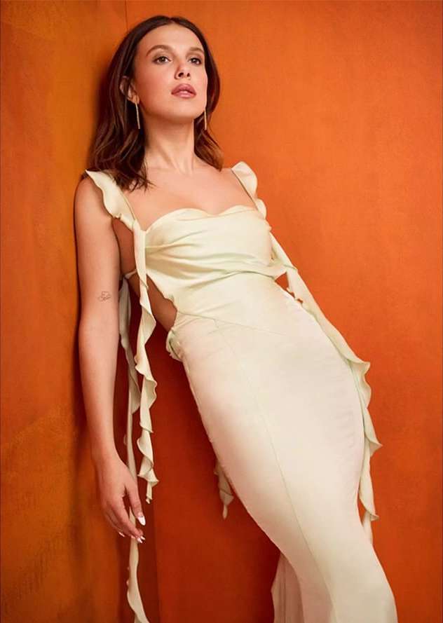 Elegant photo of an adult female in a light green gown, leaning against an orange wall. The image captures fashion and beauty elements.