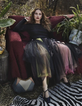 Woman with long wavy hair in a black top and multi-layered tulle skirt seated on a red sofa outdoors