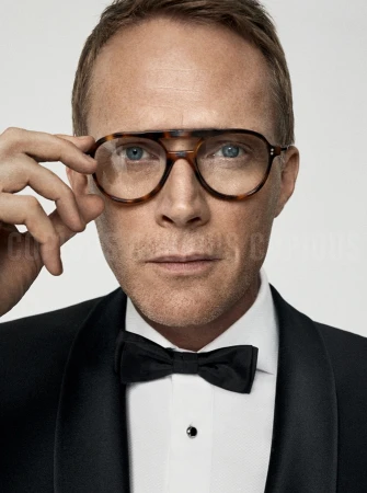 Close-up portrait of a man in a black tuxedo and bow tie wearing tortoiseshell glasses against a plain white background