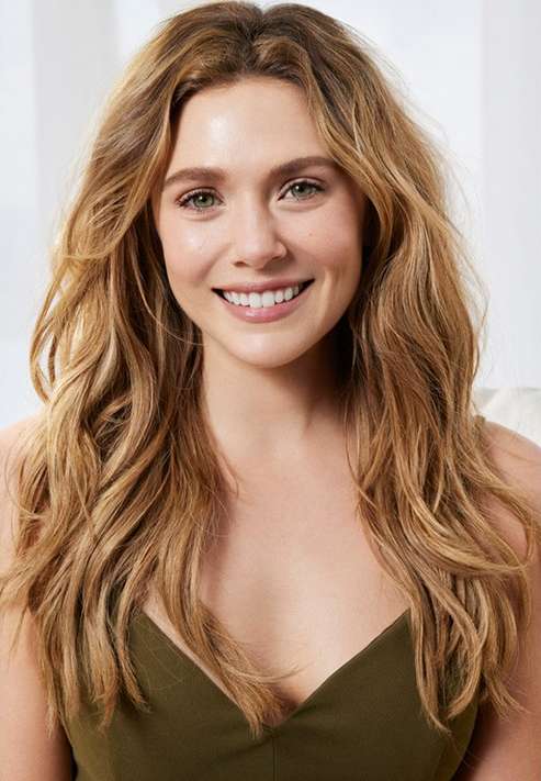 Portrait of actress Elizabeth Olsen smiling with long wavy blonde hair wearing an olive green top against a light background