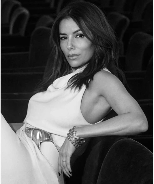 Eva Longoria poses elegantly in a black and white portrait. She is seated with her hand resting near a metallic belt.