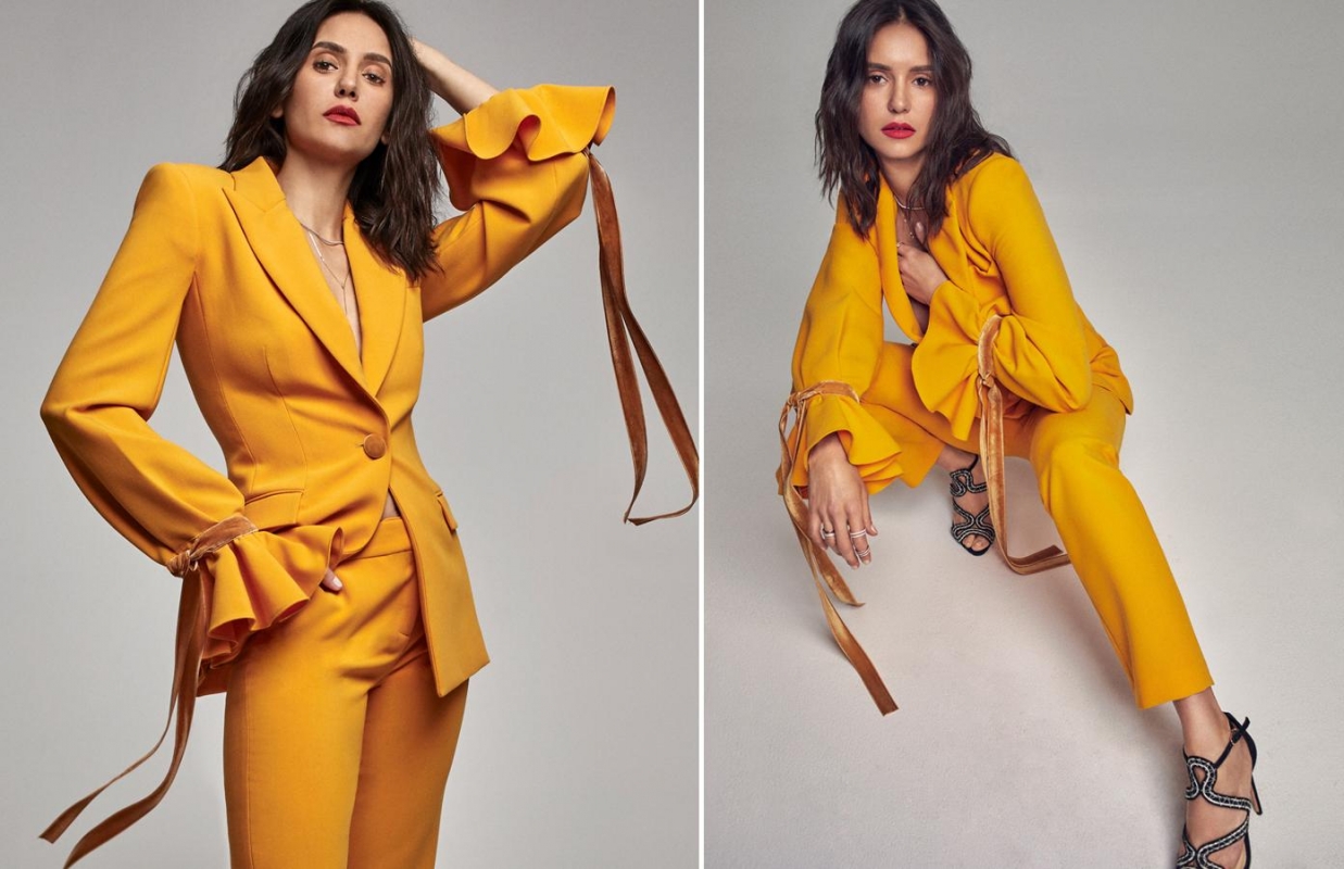 Brunette woman in a yellow suit poses in a studio, with statement sleeves and stylish high heels for a fashion-forward portrait.