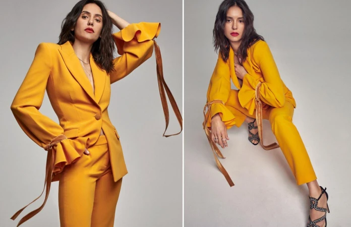 Brunette woman in a yellow suit poses in a studio, with statement sleeves and stylish high heels for a fashion-forward portrait.
