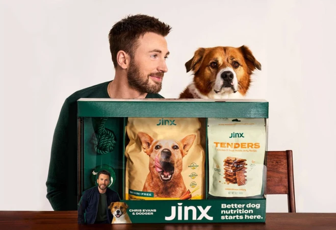 Actor Chris Evans and a dog pose behind a Jinx-brand dog food and treats display box with a photo of actor Ryan Reynolds in a studio shot.