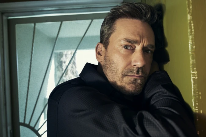Close-up portrait of Jon Hamm leaning against a doorway wearing a dark shirt, photographed by Michael Schwartz.