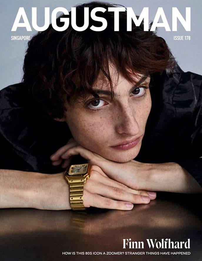 Finn Wolfhard resting his chin on folded hands wearing a gold watch in an August Man magazine cover photographed by Michael Schwartz.