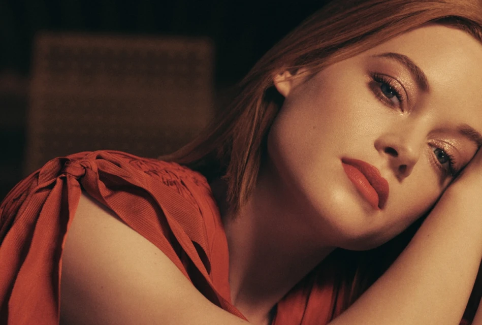 Close-up studio portrait of a young fair-skinned woman with red hair wearing a red top, showcasing red lipstick and soft lighting.