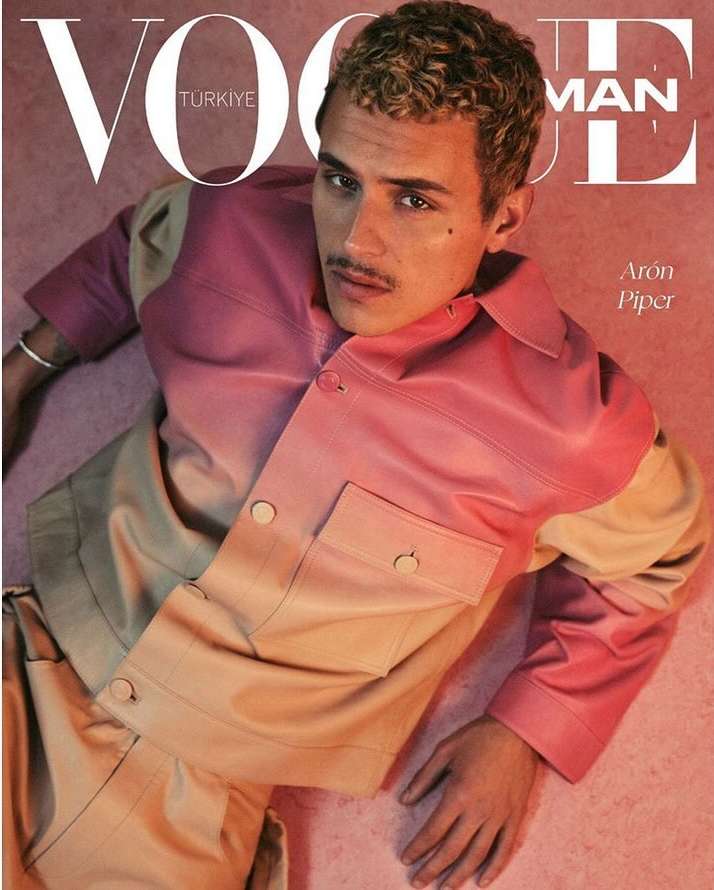 Aron Piper on the cover of Vogue Turkiye Man, wearing a pink and beige jacket and pants, posing against a matching pink backdrop.