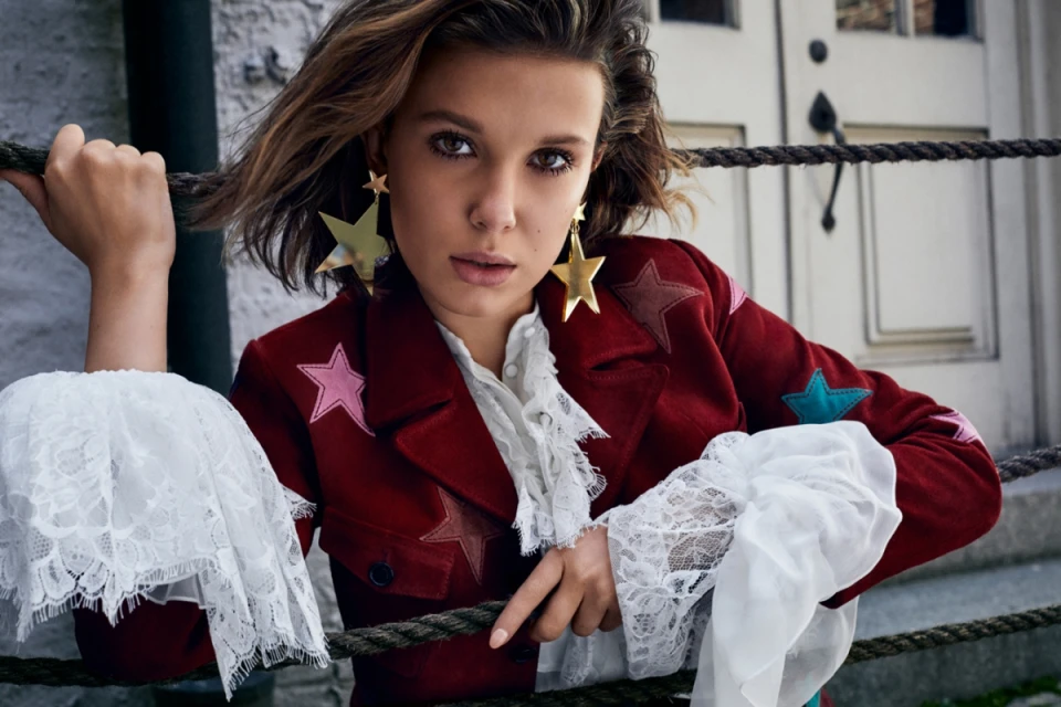 Portrait of a young adult female with short brown hair, wearing a red jacket with star patches and large gold star earrings.