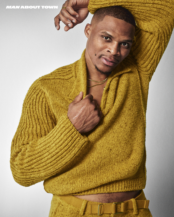 Russell Westbrook wearing a textured mustard yellow knit sweater and matching belt against a grey background.