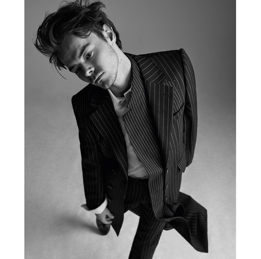 Monochrome portrait of a young man in a pinstripe suit looking downward against a neutral backdrop in a dramatic pose.
