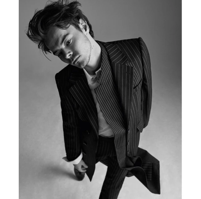 Monochrome portrait of a young man in a pinstripe suit looking downward against a neutral backdrop in a dramatic pose.