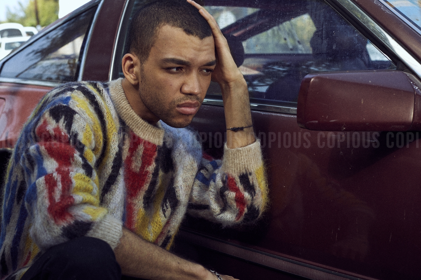Portrait of a young adult male with short hair in a colorful knit sweater sitting in a car, with a thoughtful expression.