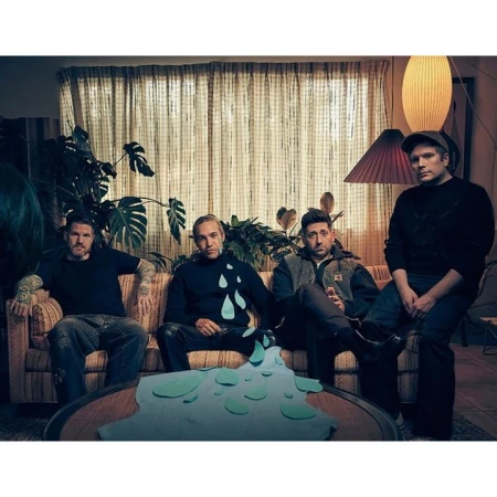 Four men sitting together on a patterned sofa in a living room with potted plants and lamps by photographer Carter Smith.