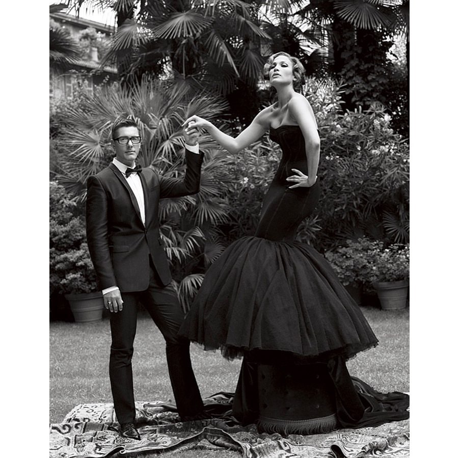 Monochrome fashion portrait featuring a woman in a black strapless gown and a man in a tuxedo standing outdoors.