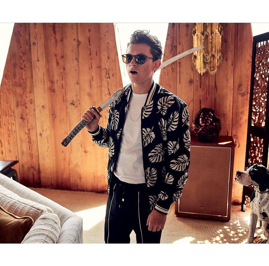 A man in a patterned jacket holds a katana sword indoors. The setting includes a couch, wood paneling, speaker, and a Dalmatian dog.
