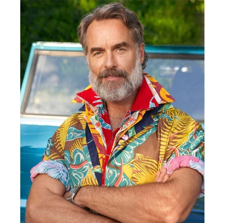 Portrait of a smiling mature man with a grey beard, wearing a brightly colored patterned shirt, standing outdoors in front of a blue vehicle.
