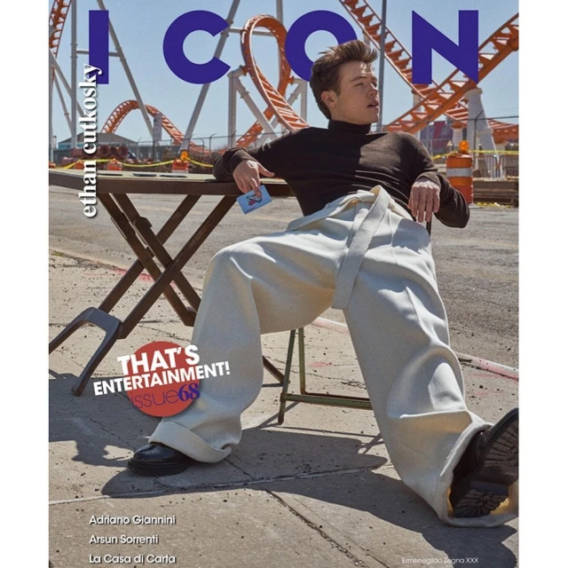 Ethan Cutkosky magazine cover: The actor lounges on a table against a rollercoaster backdrop, wearing oversized pants and a dark top.