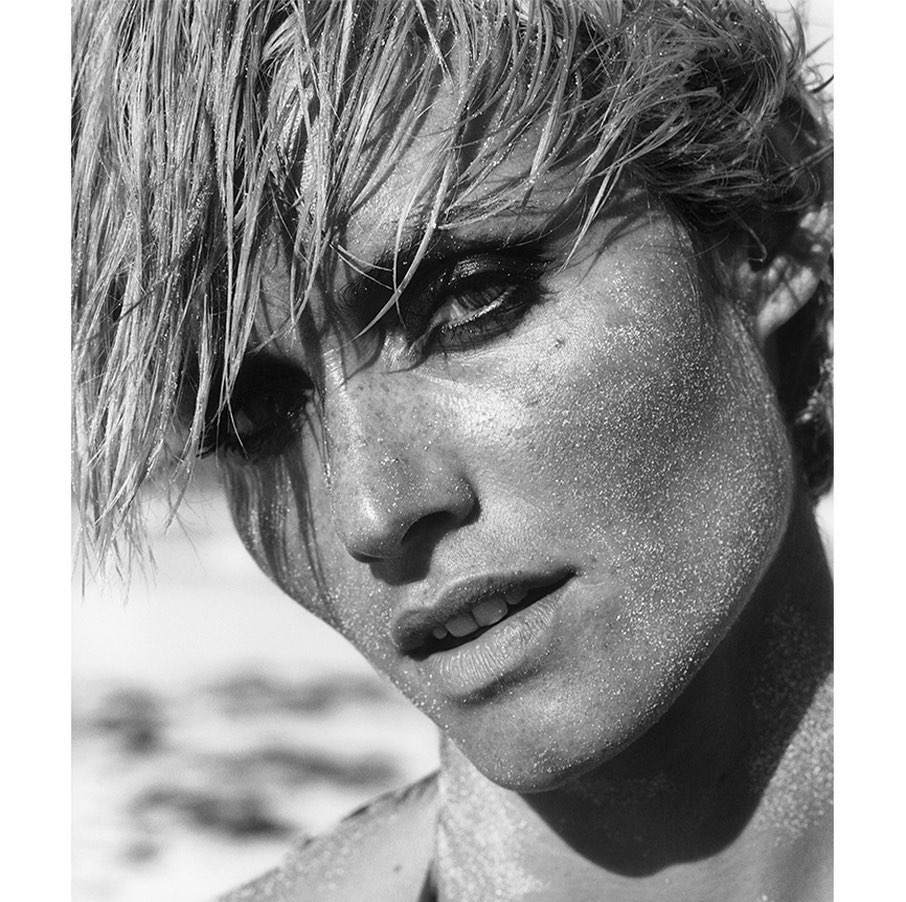 Striking black and white close-up of a female model with wet blonde hair and sparkling sand on her face at the beach.