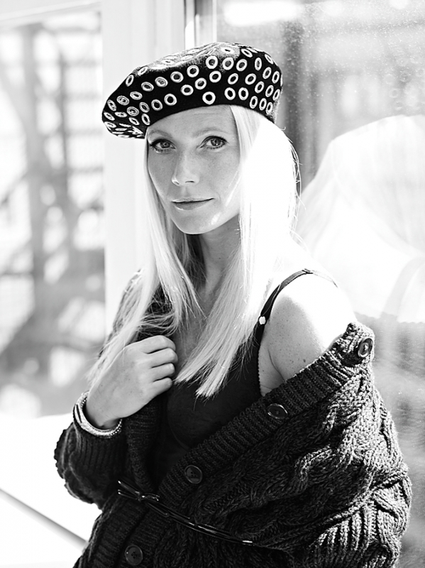 Monochrome portrait of a blonde woman wearing a black beret and cardigan, with a bright window in the background.