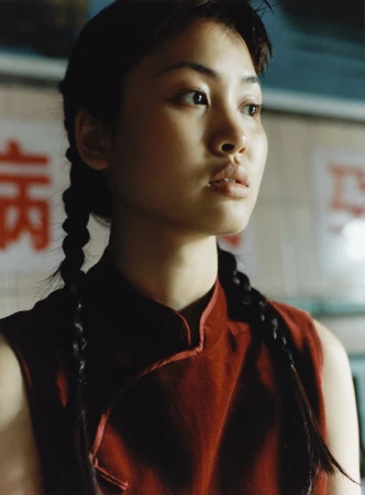 Portrait of a young woman with braided hair wearing a rust-colored sleeveless top, looking off to the side in an indoor setting.