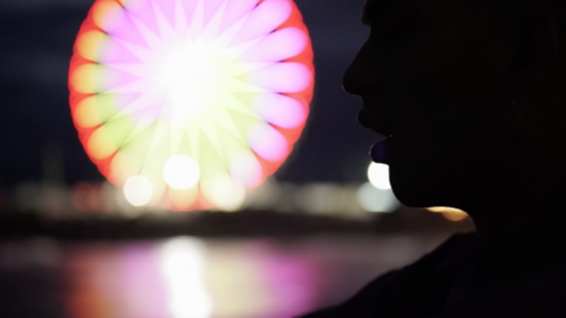 Silhouette of a person against a blurred Ferris wheel at night, capturing a moment of urban exploration and reflection in the city lights.